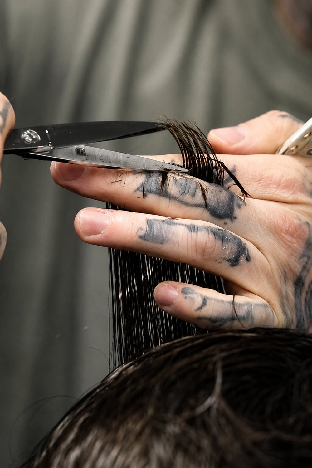 Coupe aux ciseaux, mèche tenue entre deux doigts tatoués